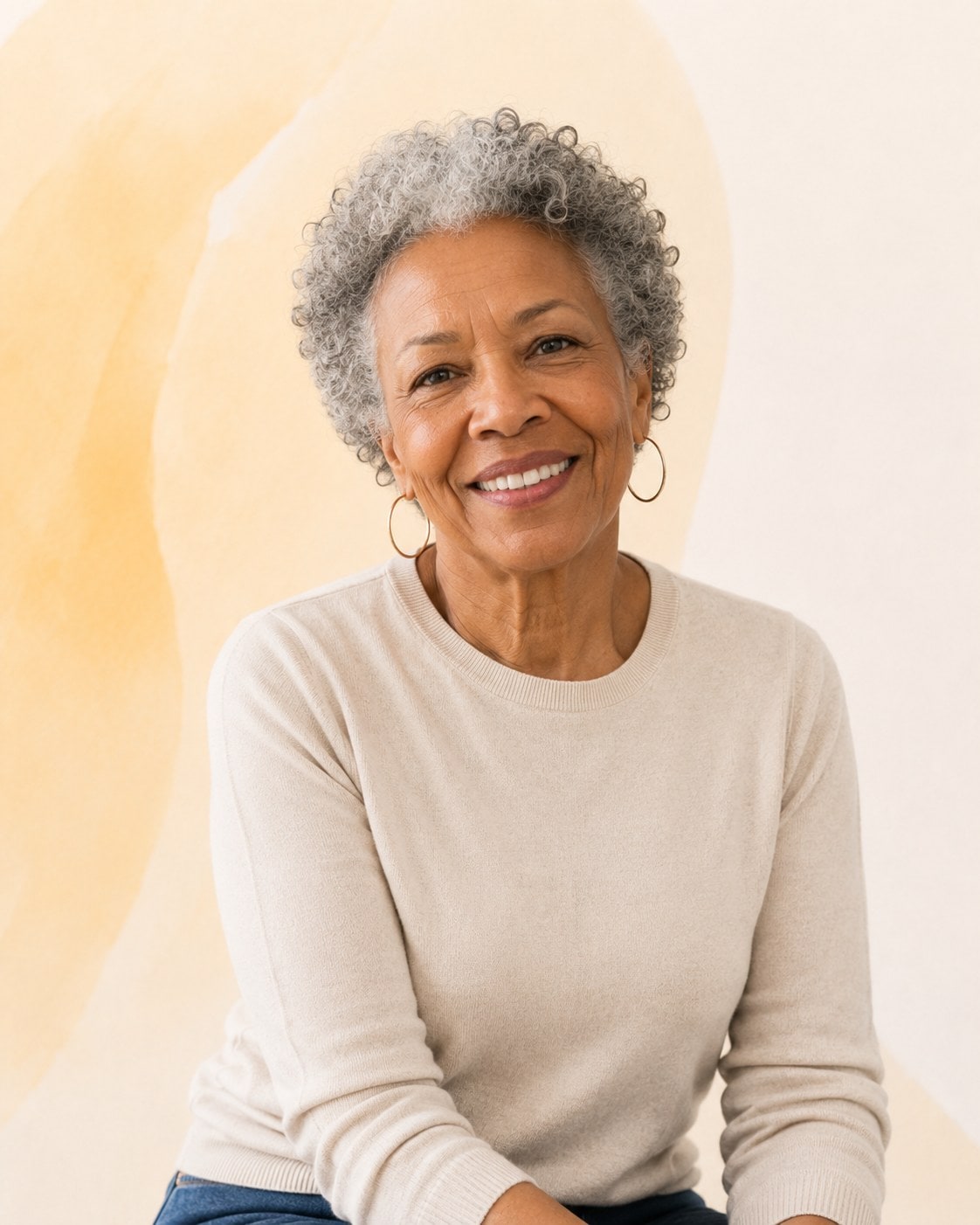 An older woman with short grey curls and gold hoop earrings, smiling broadly at the camera.