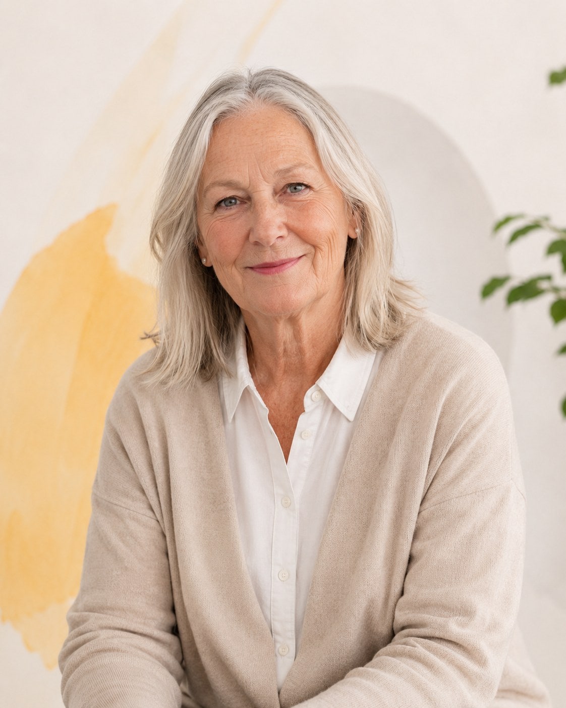 An older woman with shoulder-length white hair and a collared shirt under a soft cardigan, smiling gently.